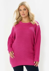 Przesadnie duży różowy sweter robiony na drutach z teksturowanym wzorem, ściągaczami przy mankietach oraz okrągłym dekoltem, z opuszczonymi ramionami i prostym dołem.
