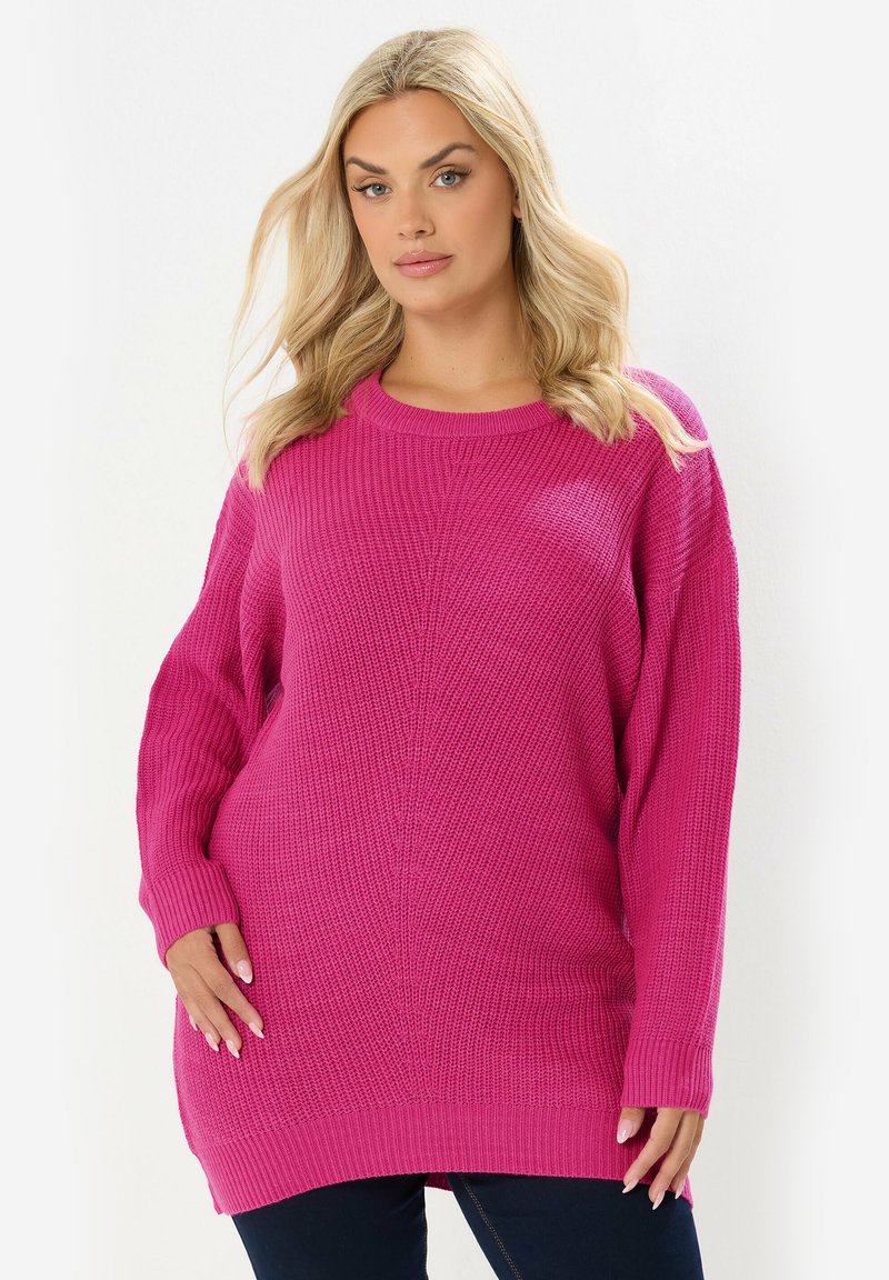 Przesadnie duży różowy sweter robiony na drutach z teksturowanym wzorem, ściągaczami przy mankietach oraz okrągłym dekoltem, z opuszczonymi ramionami i prostym dołem.