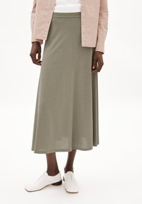 Olive green maxi skirt in soft, stretchy fabric with a smooth texture and wide waistband, paired with white lace-up shoes.