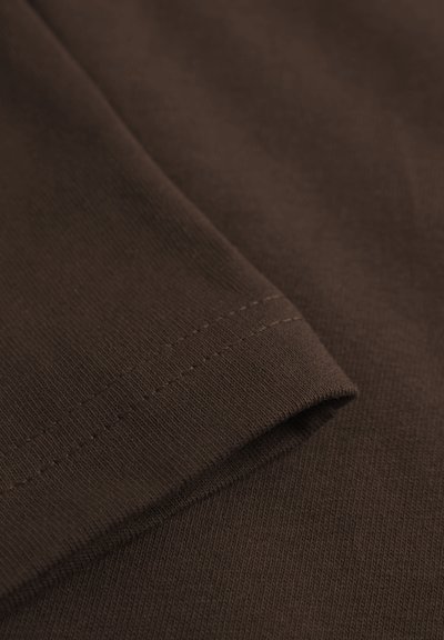 Gros plan d'un tissu marron avec une couture visible le long d'un bord replié, montrant la texture et le motif tricoté.