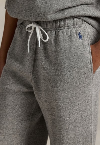 Κοντινό πλάνο ατόμου που φορά γκρι φόρμα με λευκό κορδόνι, χέρι στην τσέπη και μικρό μπλε λογότυπο Polo Ralph Lauren στο ισχίο.