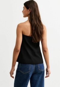 Svart, axelbandslös topp med en åtsittande design, slät textur och en kort längd, matchad med högmidjade blå jeans med bakfickor.