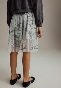 Jupe en tulle gris clair avec des détails en sequins argentés, design superposé et ballerines noires. L'ourlet plissé ajoute de la texture et du mouvement.