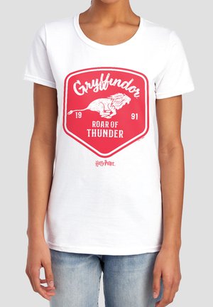 White t-shirt with red Gryffindor shield, lion graphic, text "Roar of Thunder 1991" and small Harry Potter logo worn by person in denim jeans.