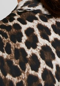 Tissu à imprimé léopard marron et noir avec une texture lisse, doté d'un col et d'une encolure ample, mettant en valeur des motifs animaliers distincts.