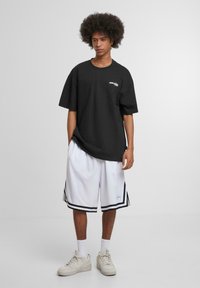 Black oversized t-shirt with a small white logo on the chest, paired with white shorts featuring black stripes, and cream sneakers.