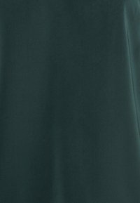 Tessuto verde scuro con una texture liscia e opaca; presenta un design semplice e privo di decorazioni e una superficie leggermente riflettente.