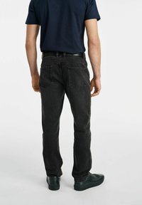 Ciemnoszare dżinsy o prostym kroju, pięć kieszeni, subtelne detale przeszycia. Noszone z czarnym paskiem i ciemnymi butami.