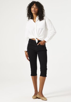 Chemise blanche à boutons avec un devant noué, jean noir cropped, et chaussures dorées à enfiler avec un motif texturé. Tissu lisse et design ajusté.