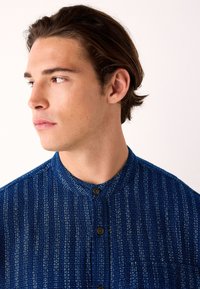 Blauw gestructureerd shirt met een mandarijnkraag, voorzien van een knoopsluiting en een patroon. De stof heeft een geweven uitstraling met een subtiele glans.