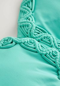 Türkizkék szövet bonyolult, csavart és hurokszerű kötélmintázattal, amely texturált díszítő mintát alkot.