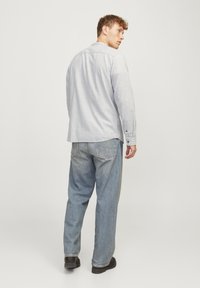 Sinine pikakäistega särk nööpide ja ümarate servadega, kombineeritud siniste laia säärega teksade ja mustade kingadega.