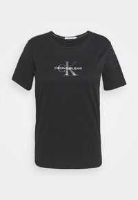 Camiseta negra de manga corta hecha de algodón, con un logo plateado de "CALVIN KLEIN JEANS" y un cuello redondo.