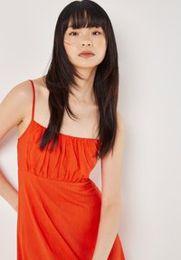 Rotes Kleid mit dünnen Trägern, gerafftem Oberteil und fließendem Rock. Der Stoff wirkt leicht und hat eine weiche Textur.