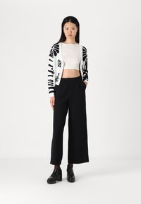 Un pantalon large noir associé à un haut blanc court et un cardigan à motifs noir et blanc. Le cardigan présente de grandes formes ressemblant à des feuilles.
