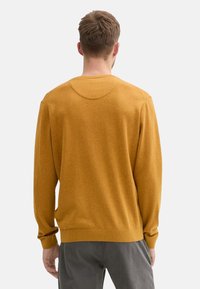 Suéter de punto amarillo mostaza con cuello redondo, mangas largas y puños acanalados; textura suave y corte relajado.