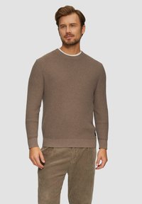 Brauner Strickpullover aus strukturiertem Stoff, mit rundem Ausschnitt und gerippten Bündchen. Kombiniert mit hellbraunen Kordhosen.