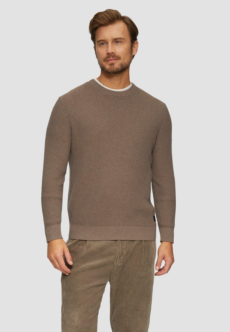 Brauner Strickpullover aus strukturiertem Stoff, mit rundem Ausschnitt und gerippten Bündchen. Kombiniert mit hellbraunen Kordhosen.