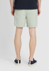 Pantaloni corti verde chiaro con una finitura tessurizzata, dotati di una tasca posteriore. Indossati con scarpe navy senza lacci e una maglietta scura.