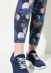 Sneakers in suede blu navy con lacci bianchi, abbinati a leggins con motivo che presenta uno sfondo scuro e cerchi colorati in viola, rosa e blu.