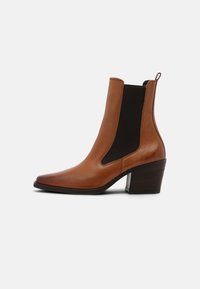 Bottine en cuir marron avec des côtés élastiques, bout pointu et talon empilé. Texture lisse avec un design élégant.