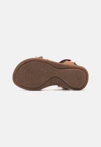 Brun sandal sula med intrikata blommönster, tillverkad av gummi. Har rundade kanter och en strukturerad yta för bra grepp.