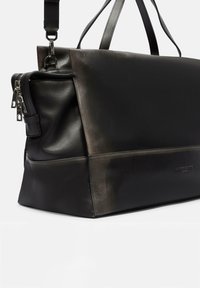 Schwarze Lederhandtasche mit glatter Textur, rechteckiger Form, Schulterriemen und mit Reißverschlüssen versehenen Fächern. Verfügt über einen subtilen Glanz und minimales Zubehör.