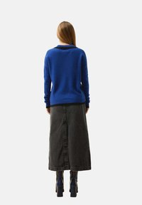 Sininen villapaita, jossa on pyöreä kaulus, päällä pitkä musta farkkuhame. Jalkineet ovat mustat korkokengät. Yksinkertainen tausta.