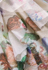 Przezroczysty materiał z kwiatowymi wzorami w odcieniach różu, zieleni i fioletu, ozdobiony złotymi kropkami i warstwową teksturą, tworzący delikatny wygląd.