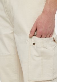 Beige textuur cargo pants met een patch pocket, enkele knop en verstevigde naden, die een functioneel en duurzaam ontwerp tonen.