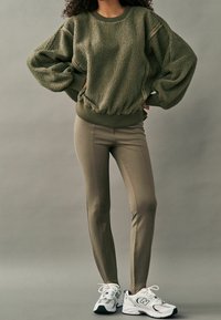 Olivengrøn fleece sweatshirt med struktureret overflade, elastisk kant og ballonærmer; parret med tætsiddende oliven leggings og hvide sneakers.