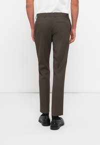 Brown tailored trousers made of textured fabric, featuring a straight leg cut, back pocket, and worn with black shoes.