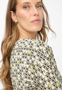 Top met een golvend patroon in groen, marineblauw en beige. Gemaakt van een lichtgewicht stof, met korte mouwen en een losse pasvorm.