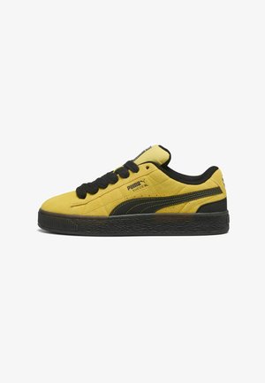 Yellow suede sneakers with black accents, featuring a textured outsole, black laces, and a prominent logo on the side.