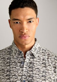 Kurzarm-Hemd mit Knopfleiste und Auto-Print-Muster, aus leichtem Stoff in Weiß- und Schwarztönen, mit spitzem Kragen und blauen Knöpfen.