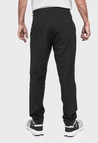 Schwarze, figurbetonte Hose mit glatter Textur, einer Gesäßtasche und verstellbaren Bündchen. Kombiniert mit grauen Sportschuhen.