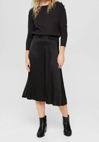 Czarny sweter z długim rękawem połączony z zwiewną czarną satynową spódnicą midi. Outfit zawiera botki za kostkę z zamkiem błyskawicznym.