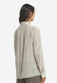 Ljust färgad långärmad skjorta med ett linjärt strukturerat mönster på ett mjukt och slätt tyg. Den har en kragkrage och knappade ärmslut.