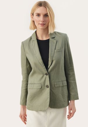 Olivový ľanový blazer so zúženým klopom, dvoma prednými vreckami a dvojitým zapínaním. Rukávy sú dlhé a jemne priliehavé.