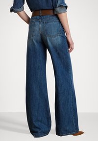 Bredde ben mørkeblå jeans laget av denim, med middels høyde, to baklommer og en subtil gradienteffekt mot kanten.