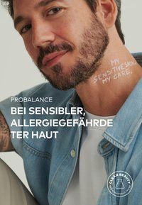 Denim jacket with a light blue hue, worn over a white shirt. Skin visible on the neck has text written in white: "MY SENSITIVE SKIN. MY CARE."