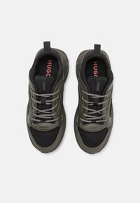 Sneakers verde scuro e neri con finiture in rete e lisce, caratterizzati da lacci grigi e un'etichetta sulla linguetta che recita "HUGO."