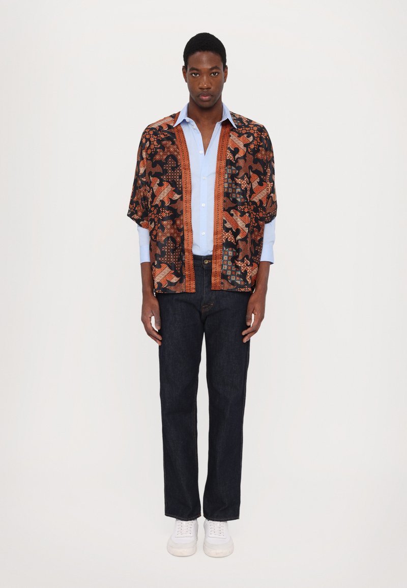 Zwart-oranje gestreepte kimono over een lichtblauw shirt, gecombineerd met donkere jeans en witte sneakers. Heeft gedurfde graphics en een relaxte pasvorm.