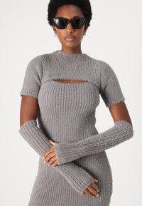 Robe tricotée grise à manches courtes, avec une découpe au niveau de la poitrine. Accompagnée de chauffe-poignets longs assortis. Texture douce.