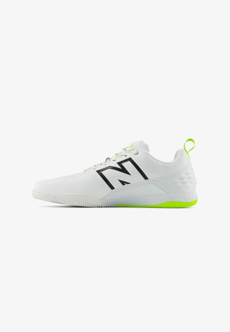 White athletic shoe with black logo, textured upper, and bright green accents on the sole and heel. Features lace-up design and pull tab.