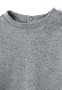 Camiseta gris de cuello redondo hecha de una tela suave con una textura sutil, que presenta un pequeño detalle de botón en la parte trasera del escote.