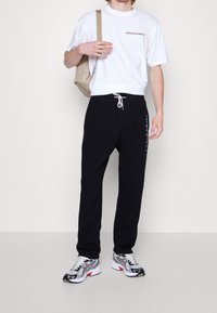 Camiseta blanca de algodón con "ABERCROMBIE" impreso; pantalones de chándal negros con cintura elástica; zapatillas grises y negras con acentos rojos.
