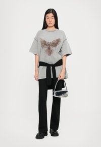 Grijze oversized t-shirt met een adelaar grafiek, gecombineerd met zwarte high-waisted broek en een kleine zilveren handtas. Zwarte riem knoop in de taille.