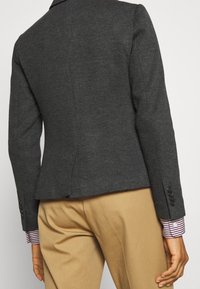 Mörkgrå skräddarsydd kavaj med en strukturerad silhuett, med knappade manschetter och en peplumdesign, i kombination med en randig skjorta vid ärmen.