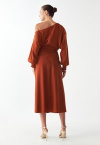 Hrdzavohnedá, stredne dlhá šaty s off-shoulder dizajnom, nariasanými rukávmi a splývavou siluetou. V kombinácii so sandálmi na opätku.